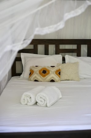 Un lit bien fait, avec du linge de lit blanc, une tête de lit en bois et un coussin décoratif orné d’un motif géométrique.