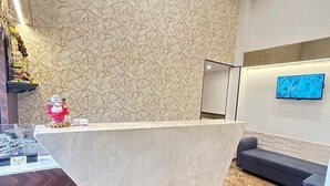 A reception area with a marble-patterned wall, a reception desk, a blue sofa, and a modern chandelier. - Hotel MIG SUITES (Mumbai)
