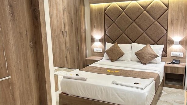A modern bedroom with a bed, wooden headboard, bedside lamps, and a wooden wardrobe. - Hotel MIG SUITES (Mumbai)