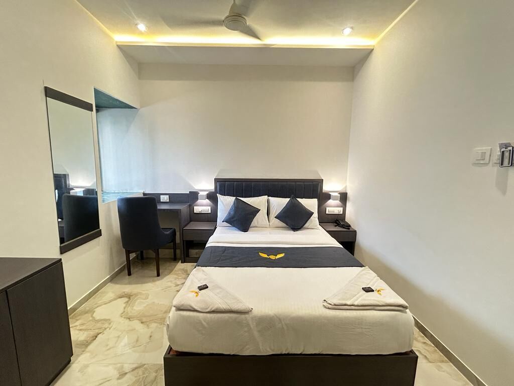 A hotel room with a bed, bedside tables, a desk, a chair, a mirror, and a ceiling fan.