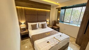 A modern bedroom with a large bed, bedside lamps, a wooden headboard, and a window with a view. - Hotel MIG SUITES (Mumbai)