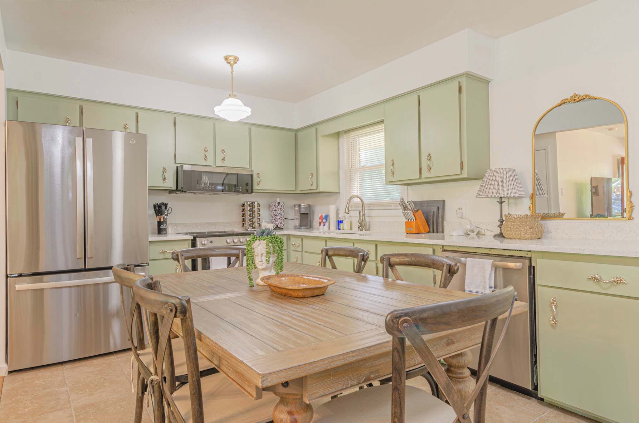 A kitchen with green cabinets, stainless steel appliances, a wooden dining table, and a chandelier.