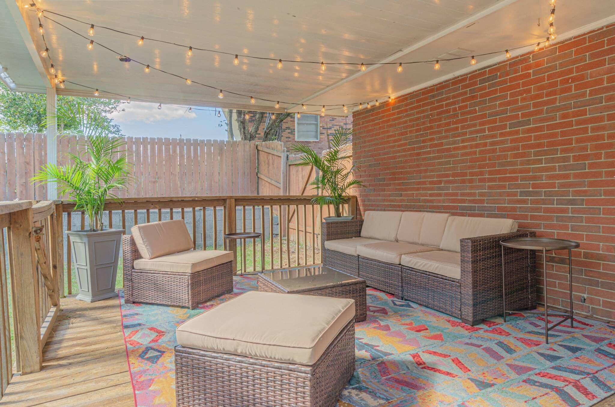 An outdoor patio with wicker furniture, a colorful rug, and string lights.