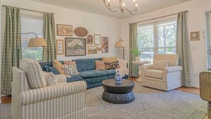 Un salon avec un canapé bleu, des fauteuils à rayures, une table basse ronde et un lustre.