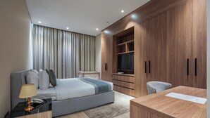 Una habitación de hotel moderna con cama, mesita de noche, lámpara y un escritorio de madera con una silla.
