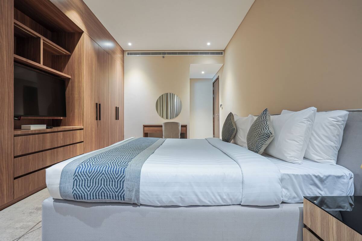 A modern bedroom with a large bed, built-in TV, and wooden cabinetry.