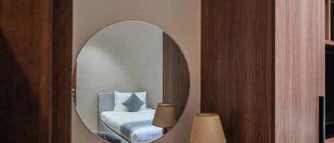 A round mirror reflecting a bed with pillows and a bedside lamp.