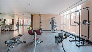 Un gimnasio amplio con diversos equipos de ejercicio, ventanas grandes y una zona de recepción con asientos.