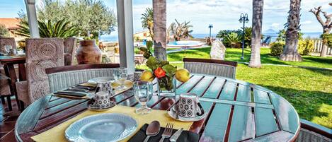 Ein runder Holztisch, gedeckt für ein Essen, mit Blick auf das Meer und Palmen.