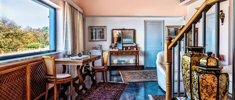 A room with a large window, a wooden desk, a chair, a sofa, and a staircase with a railing.
