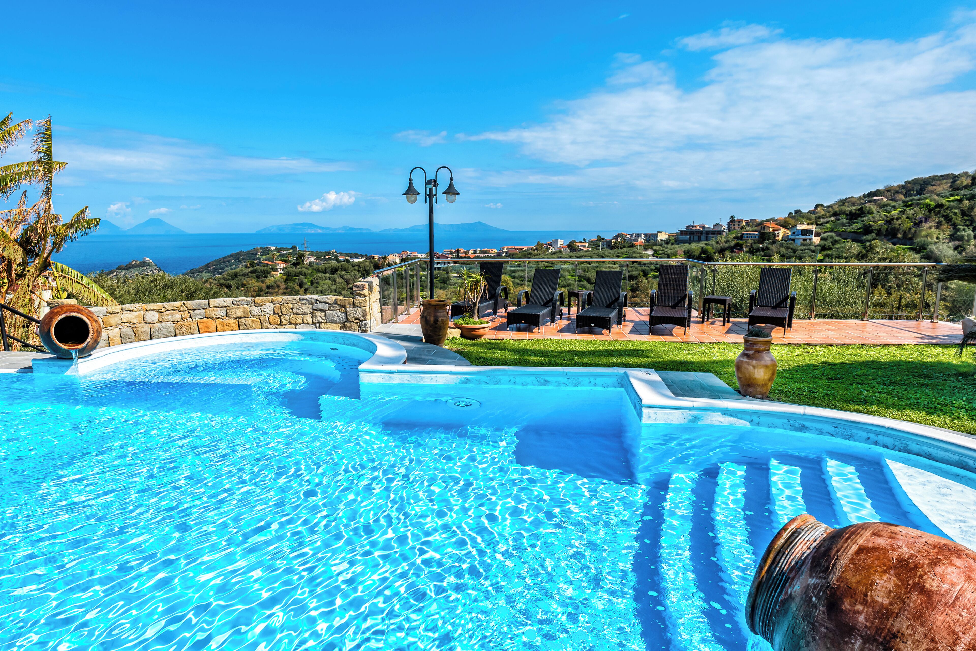 A swimming pool with clear blue water, surrounded by lounge chairs and a stone wall.