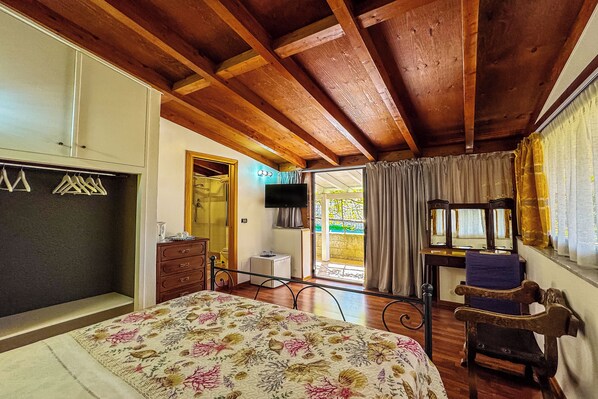 A bedroom with a bed, wooden ceiling beams, a wardrobe, a dresser, a mirror, and a window with curtains. - Villa Bency (Capo d'Orlando)