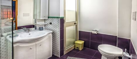 Un baño con lavamanos blanco, espejo e inodoro, azulejos morados y un taburete pequeño.