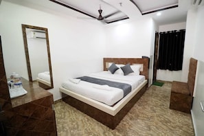Une chambre d’hôtel avec un lit, une table de chevet avec des bouteilles d’eau, un miroir, un ventilateur de plafond et un rideau noir.