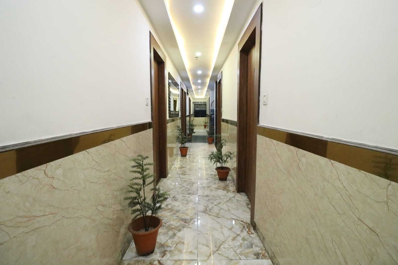 Un largo pasillo bien iluminado con suelo de mármol y puertas de madera, adornado con plantas en macetas a los lados.