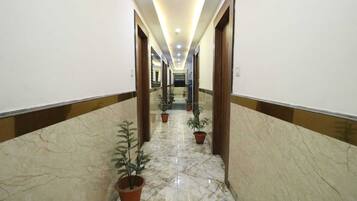 Un largo pasillo bien iluminado con suelo de mármol y puertas de madera, adornado con plantas en macetas a los lados.