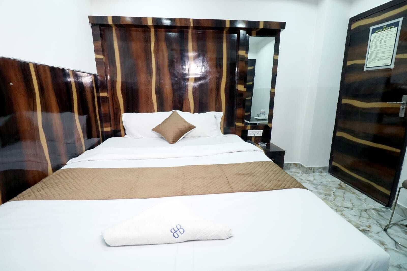 A hotel room with a bed, a nightstand, a mirror, and a door with a sign.