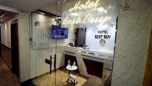 A hotel reception area with a modern design, featuring a reception desk, a television, and a neon sign that reads "Hotel Best Buy." - hotel best buy (Kolkata)