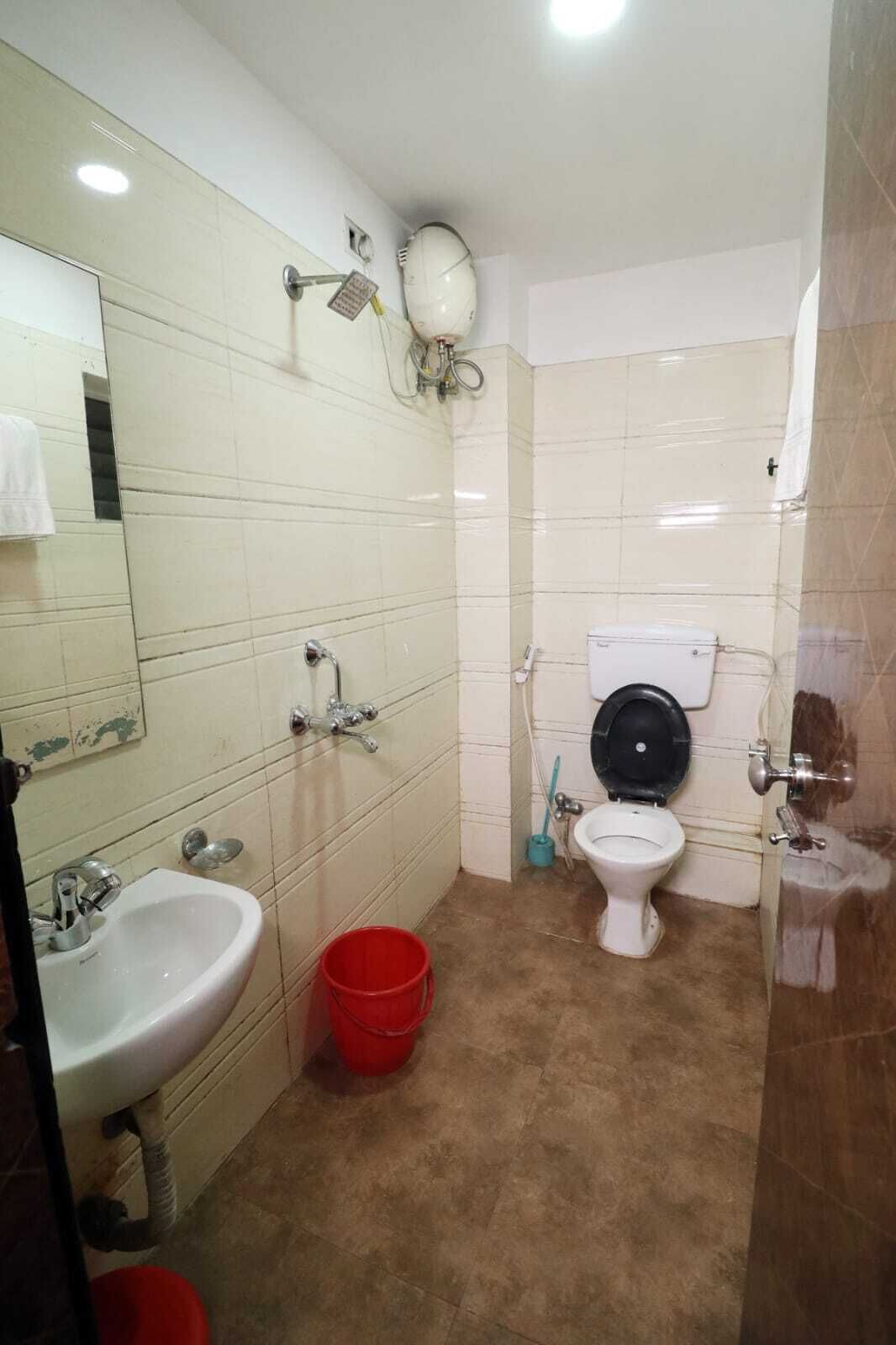 Een badkamer met een wastafel, toilet en spiegel. Er staat een rode emmer op de vloer.