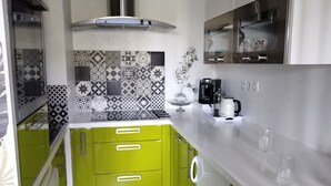 A kitchen with green cabinets, a stainless steel range hood, a tiled backsplash, and a coffee maker. - Apartment 44 m2. Type 2 (Aix-en-Provence)