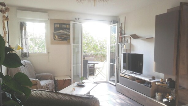 A modern living room with a sofa, a coffee table, and a TV. There is a sliding glass door leading to an outdoor area with a table and chairs. - Apartment 44 m2. Type 2 (Aix-en-Provence)