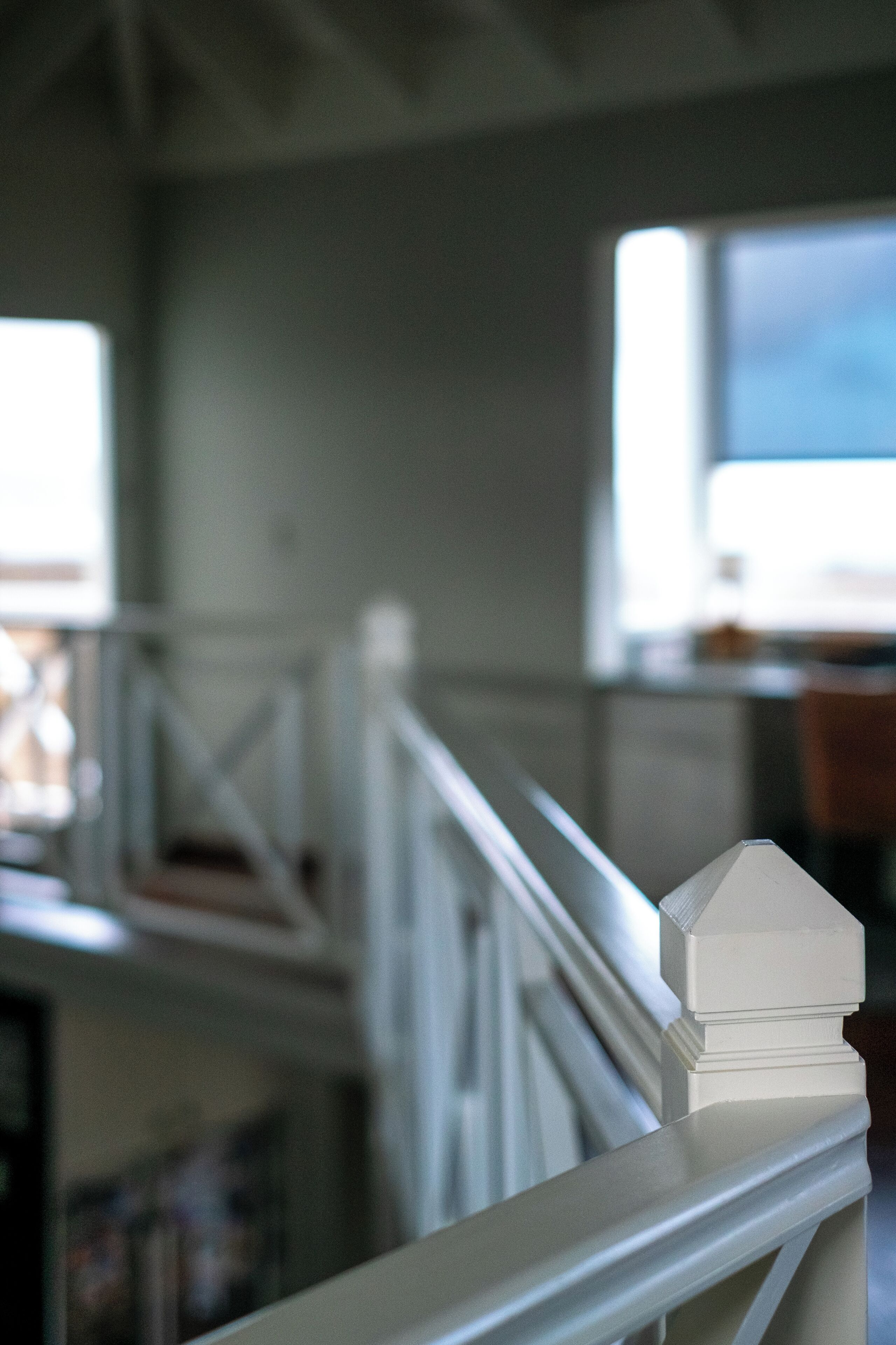 Een witte balustrade met een klein wit object erop, een trap op de achtergrond en een raam met uitzicht.