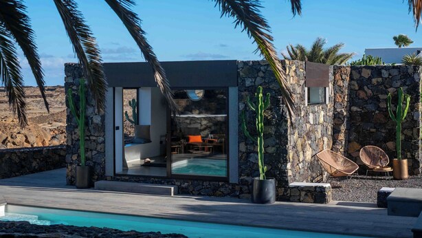 A modern villa with a stone exterior, a glass door leading to a pool area, and outdoor seating. - Villa by the Sea (Haria)