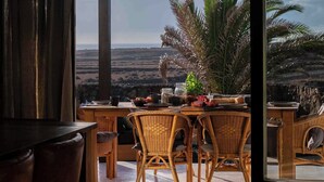 A room with a large window overlooking a landscape, wicker furniture, and a view of palm trees. - Villa by the Sea (Haria)