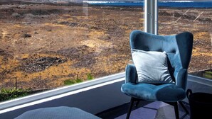 A room with a large window offering a view of a barren landscape with distant mountains and a body of water. - Villa by the Sea (Haria)