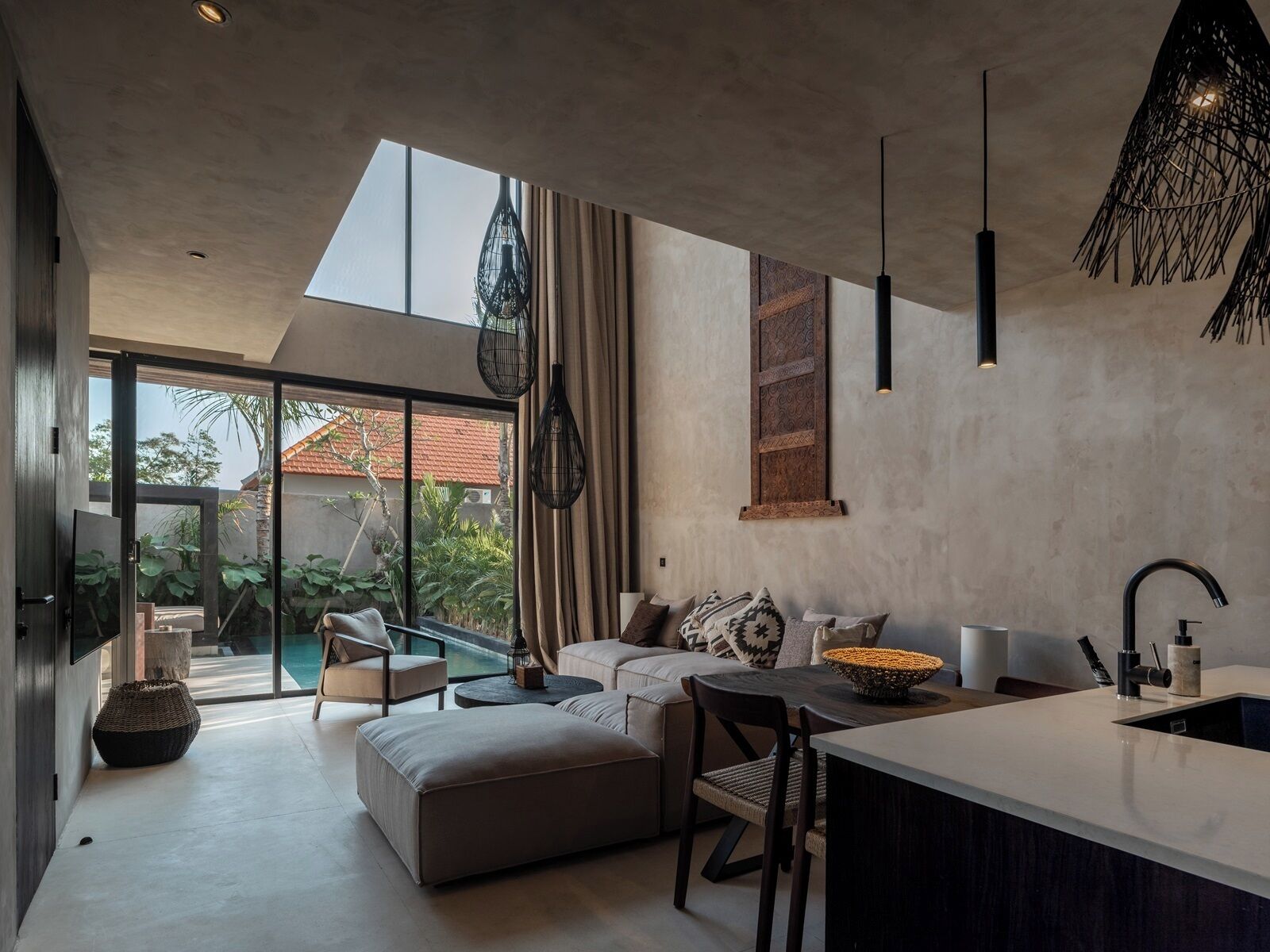 Een moderne keuken met een groot eiland, een zithoek met een bank en stoelen, en uitzicht op een zwembad en groen buiten.