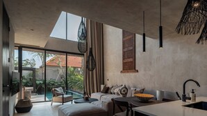 Una cocina moderna con una isla grande, un comedor con sofá y sillas, y vistas a una piscina y zonas verdes al exterior.
