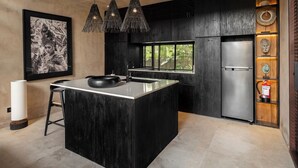 Cocina moderna con una isla central, luces colgantes, un refrigerador y una ventana con vista a follaje.
