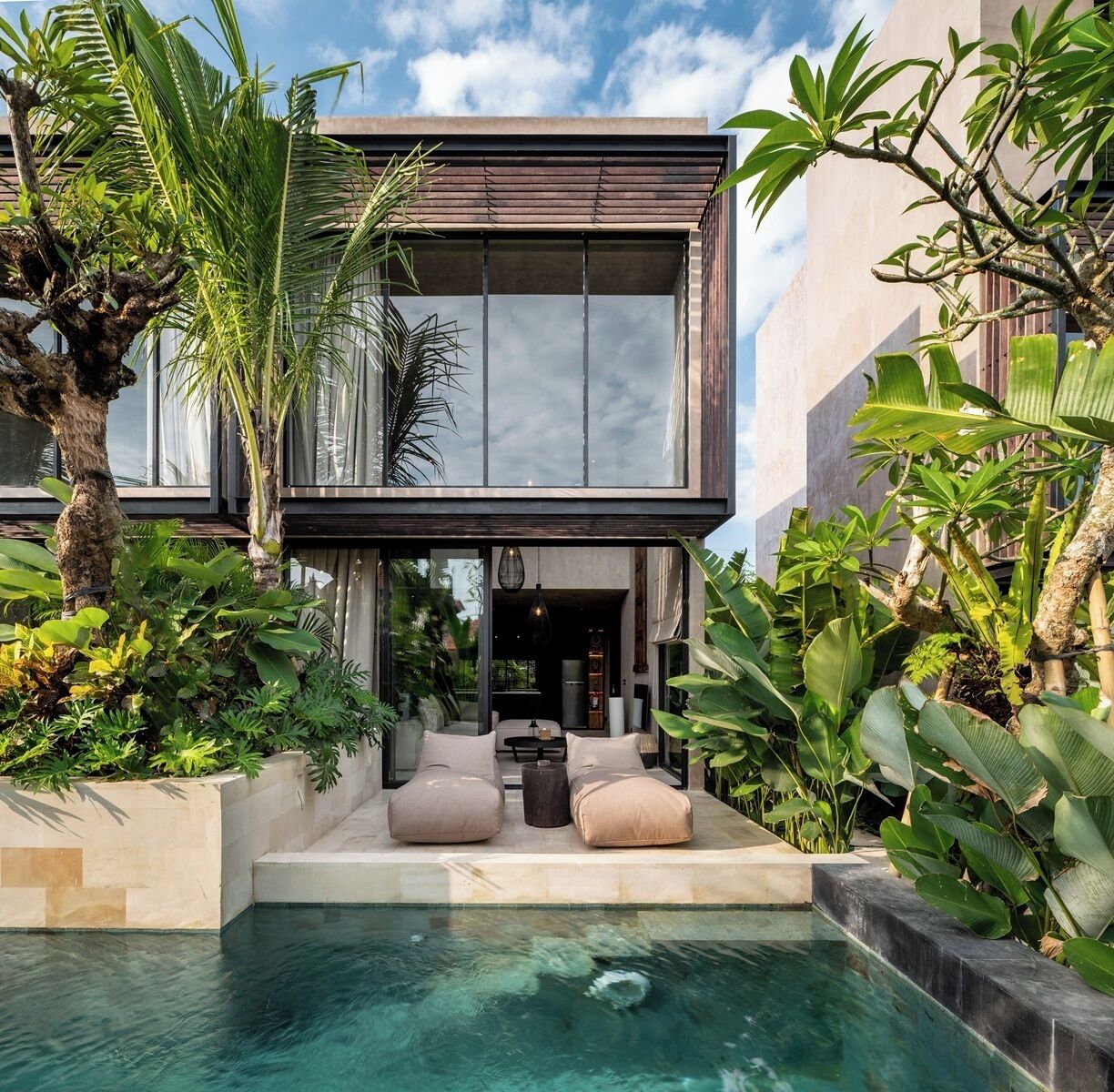 A modern two-story house with a swimming pool, surrounded by lush tropical plants.