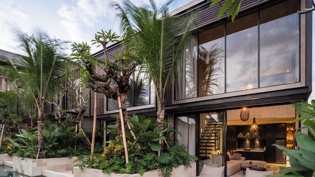 Una casa moderna con piscina, mobiliario de exterior y abundante vegetación.
