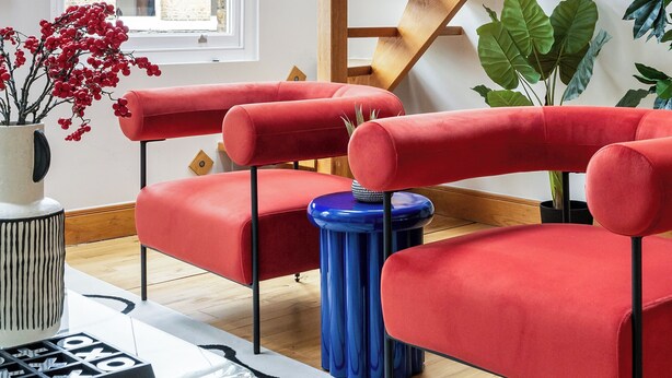 A modern living room with a wooden staircase, red chairs, a chandelier, and a large window with a view of buildings. - Vibrant Urban Escape, Family Friendly - Sleeps 8! (London)