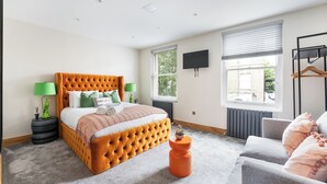 A bedroom with a tufted orange bed, grey armchair, and a small orange stool. - Vibrant Urban Escape, Family Friendly - Sleeps 8! (London)