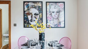 A dining area with a table set for four, featuring modern chairs and a vase with yellow flowers. Two framed artworks are displayed on the wall above the table. - Vibrant Urban Escape, Family Friendly - Sleeps 8! (London)