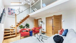 A modern living room with a staircase, red chairs, a glass coffee table, and a grey sofa. - Vibrant Urban Escape, Family Friendly - Sleeps 8! (London)