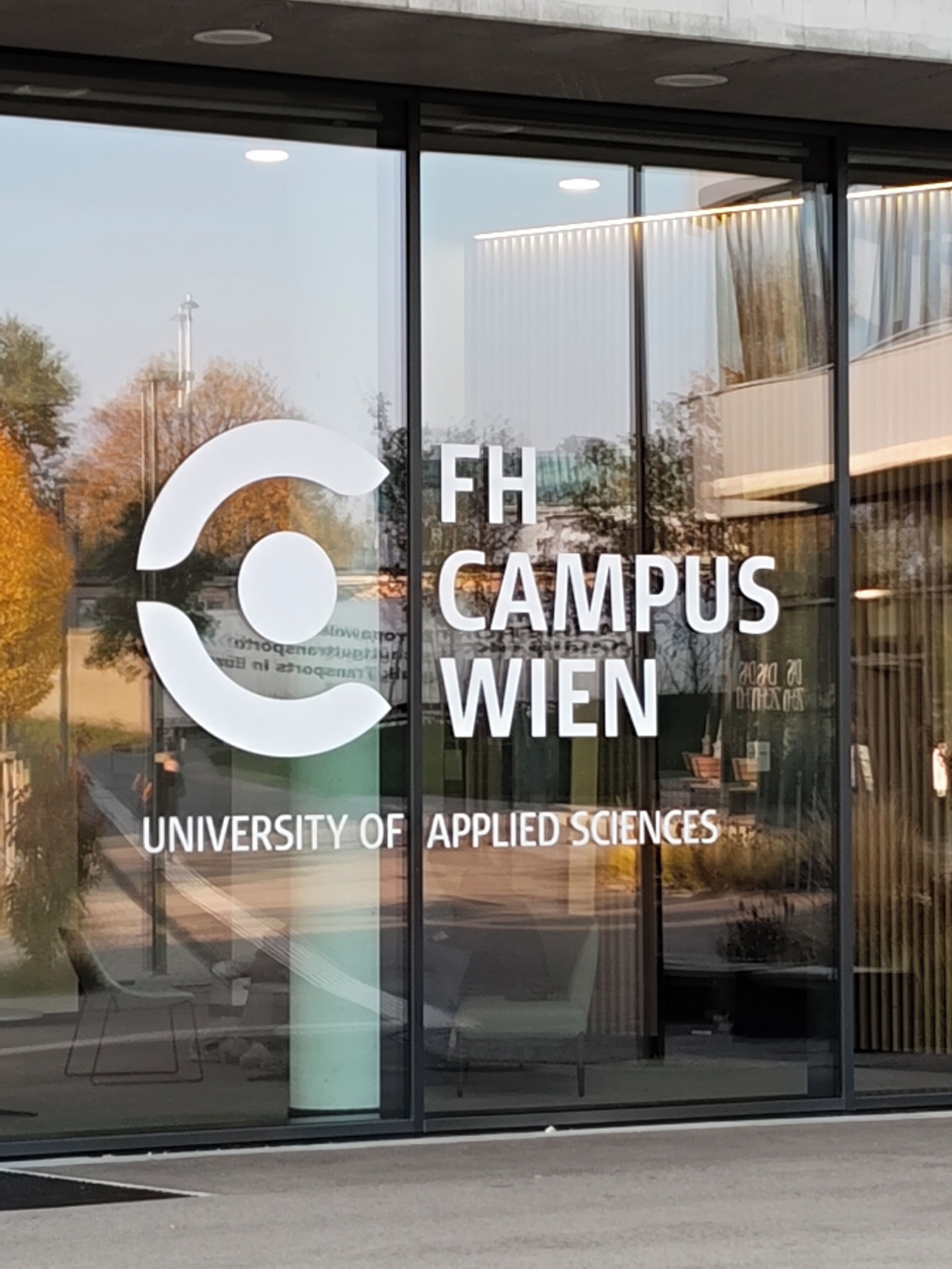 A building with a large glass window displaying the text "FH CAMPUS WIEN UNIVERSITY OF APPLIED SCIENCES".