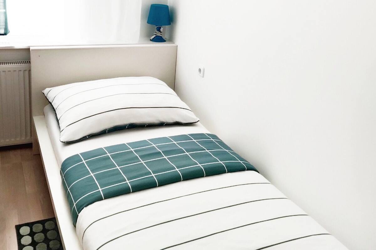 Una cama pequeña y bien arreglada con una colcha a rayas y un almohadón verde.