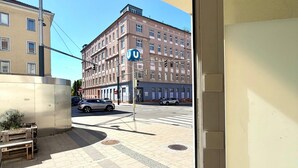 Uitzicht vanaf een balkon op een straat met een gebouw met een blauw bord, een zebrapad en geparkeerde auto's.