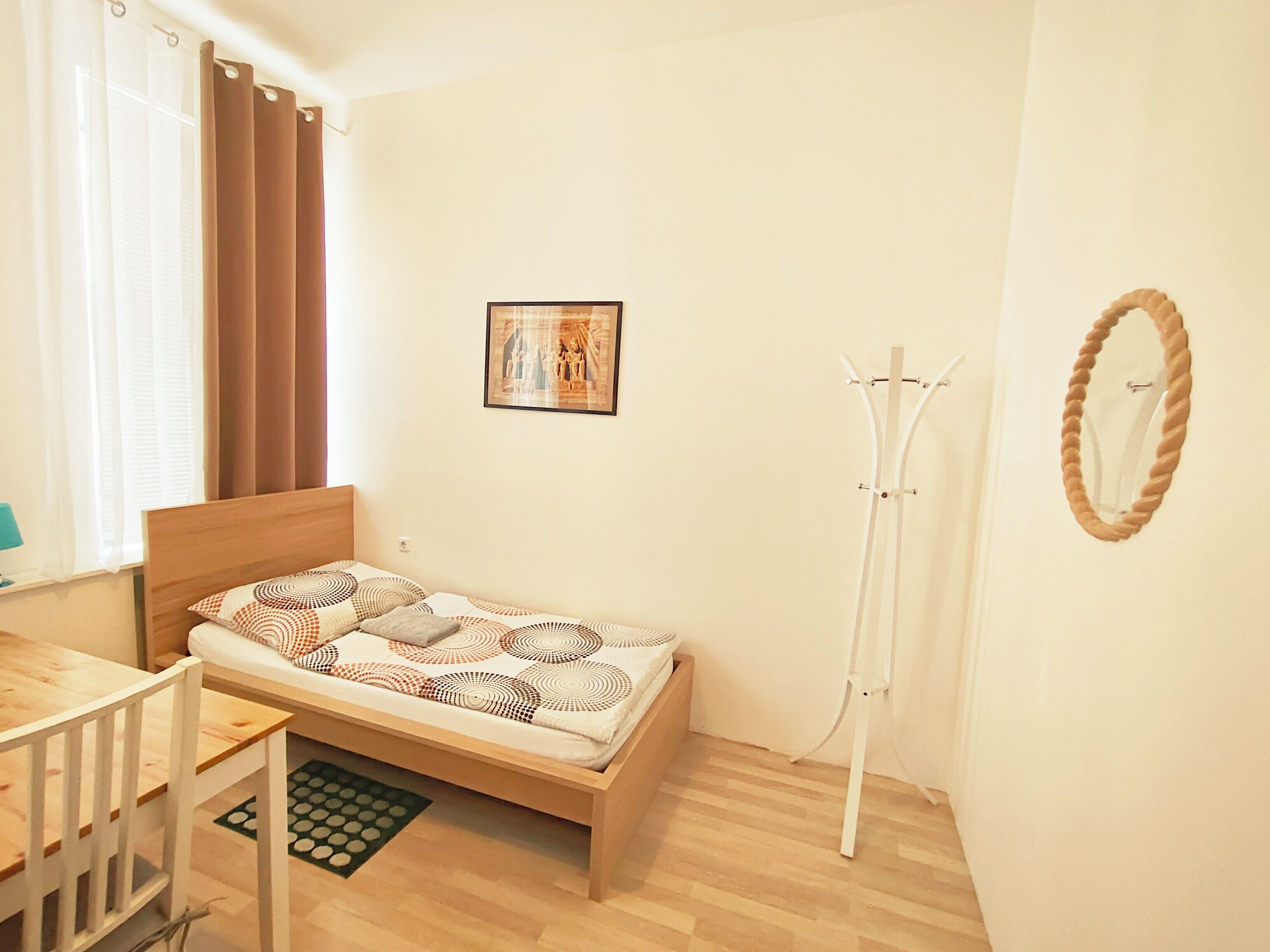 Un dormitorio con cama, una silla, perchero y un cuadro en la pared.