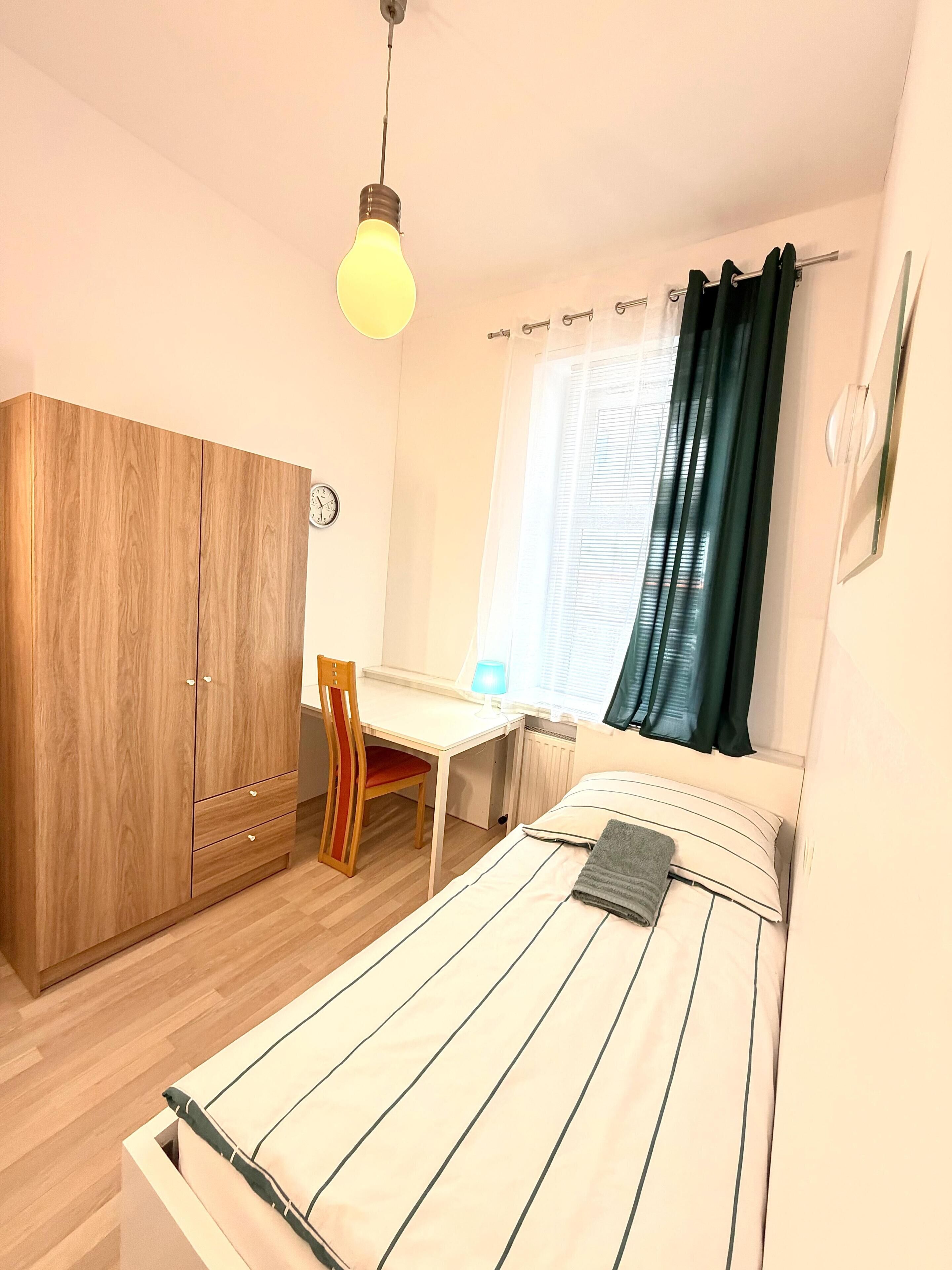 A bedroom with a bed, a desk, a chair, a wardrobe, and a window with curtains.