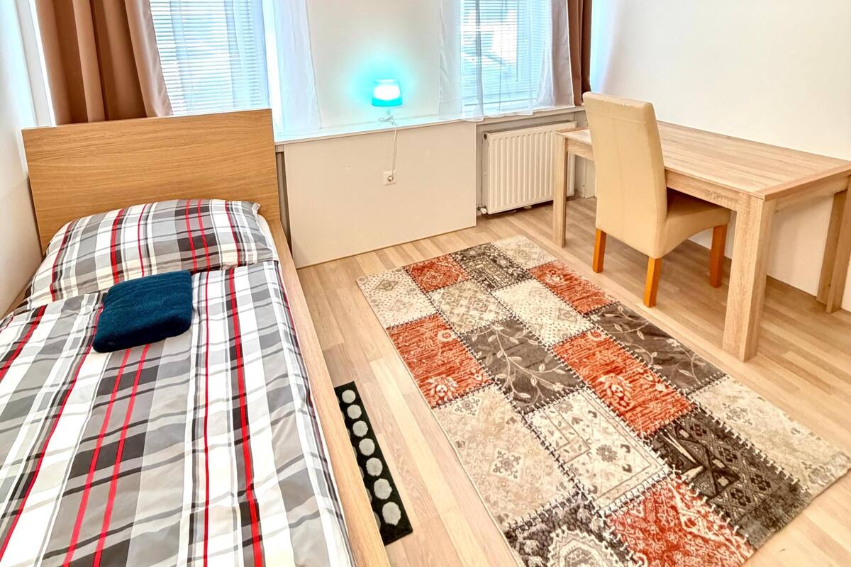 Un dormitorio con cama, escritorio, silla y vistas al exterior.