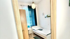 Een slaapkamer met een bed, een bureau, een stoel, een plafondlamp en een raam met gordijnen.