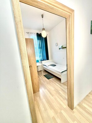 Un dormitorio con cama, escritorio, silla, lámpara en el techo y ventana con cortinas.
