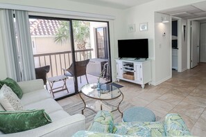 A living room with a sofa, a glass coffee table, a TV, and a balcony with a chair.