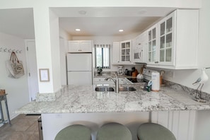 A modern kitchen with white cabinetry, a granite countertop, and a built-in sink.