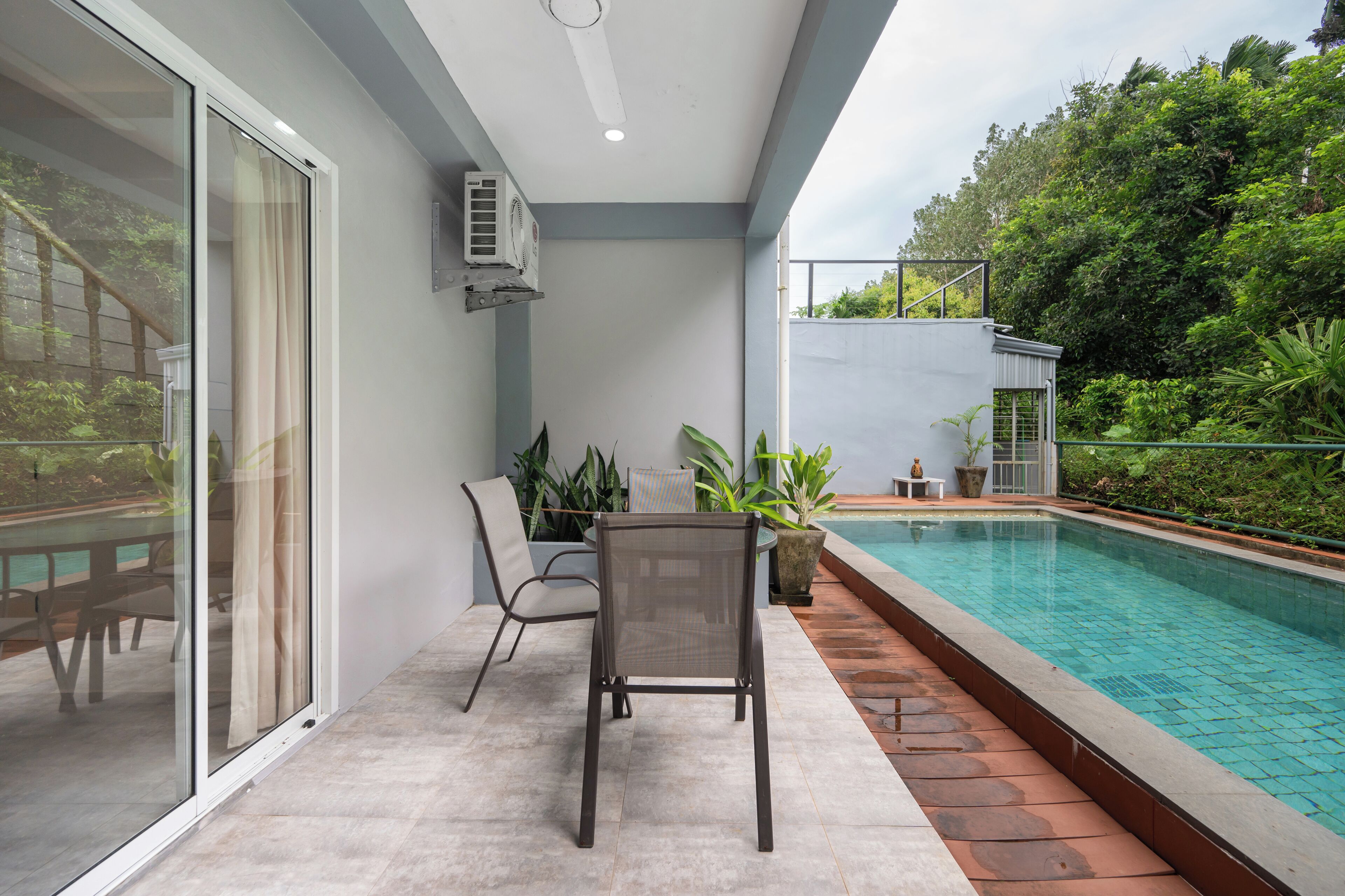 Un espacio exterior moderno con piscina, puerta de cristal que da a un balcón y una zona de estar con una silla y una mesa.