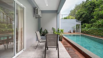 Un espacio exterior moderno con piscina, puerta de cristal que da a un balcón y una zona de estar con una silla y una mesa.